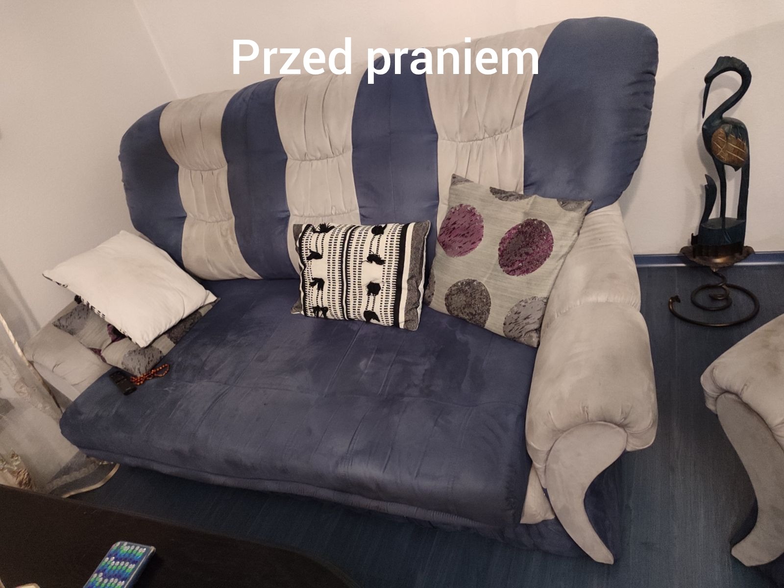Zdjęcie sofy z poduszkami przed czyszczeniem. Widoczne plamy i zabrudzenia na tapicerce w kolorze niebieskim. Sofa w salonie.
