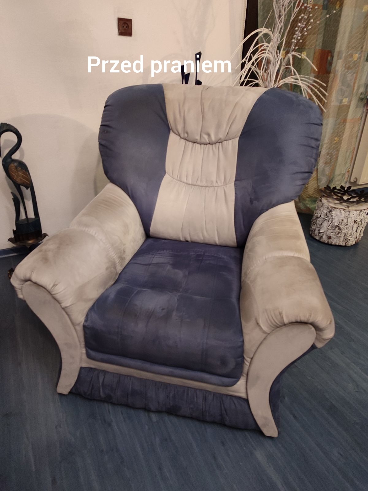 Zabrudzony, dwukolorowy fotel tapicerowany (niebiesko-kremowy) z widocznymi plamami na siedzisku i podłokietniku, sfotografowany z bliska przed czyszczeniem.