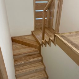 Stolarstwo Adam Pilch - Jasne, drewniane schody z balustradą, z widocznym fragmentem drzwi z poziomymi przeszkleniami, prowadzące do górnej kondygnacji. Widok z góry.