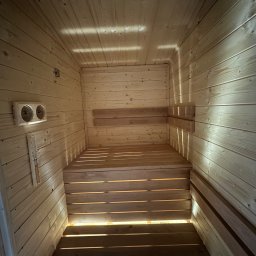 Struktura drewna - Wnętrze sauny z jasnego drewna, widok z dołu na ławy i ścianę z termometrem. Naturalne światło podkreśla strukturę drewna.