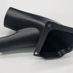 Czarny, matowy element z tworzywa sztucznego o rozwidlonej strukturze i kwadratowym kołnierzem z otworami, leżący na białym tle.