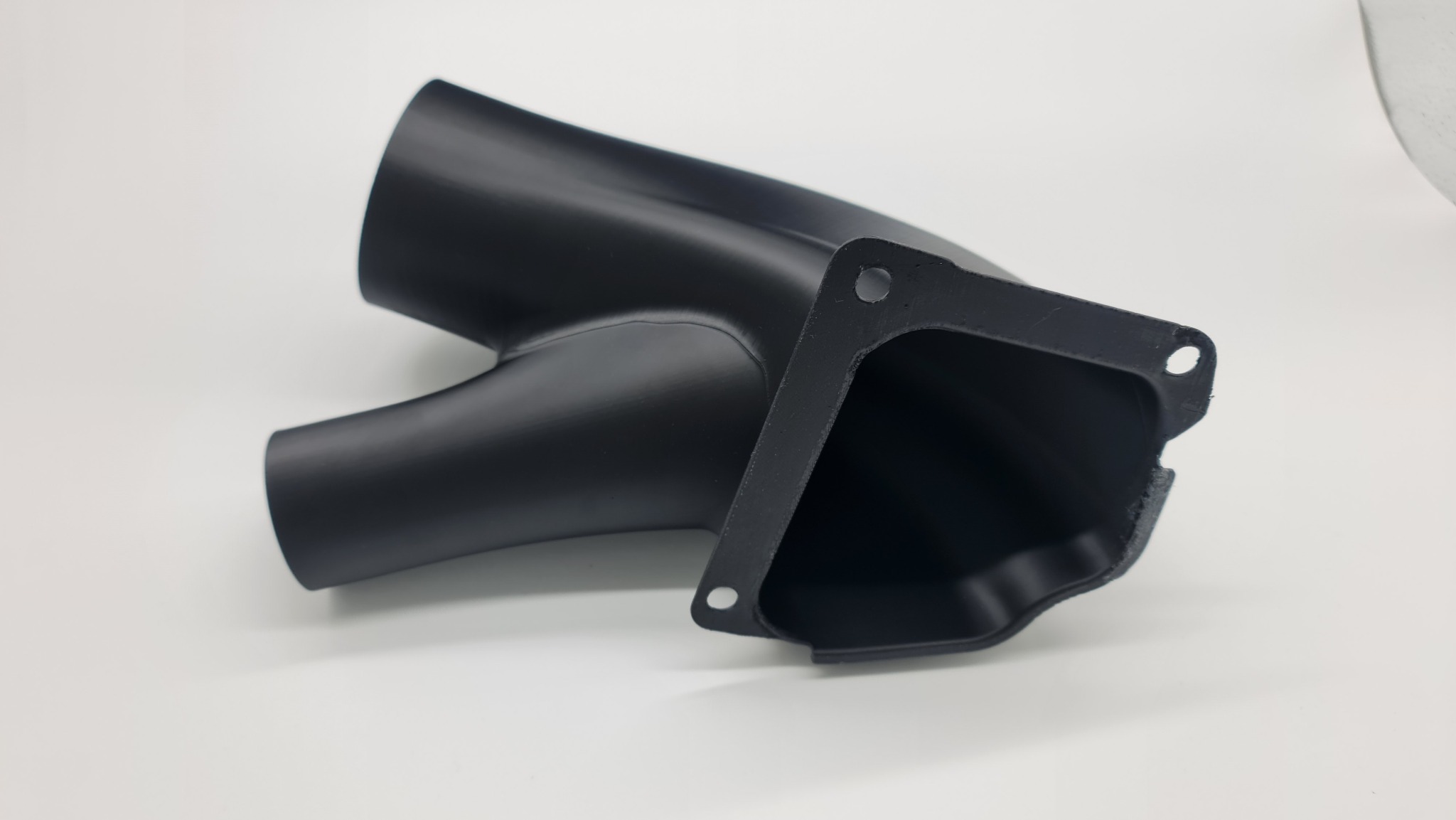 Czarny, matowy element z tworzywa sztucznego o rozwidlonej strukturze i kwadratowym kołnierzem z otworami, leżący na białym tle.