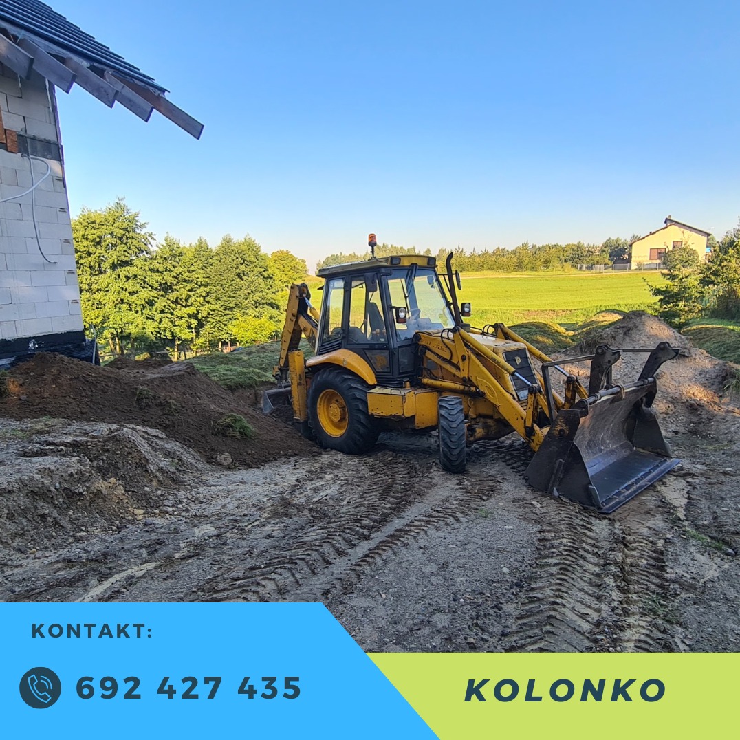 Żółta koparko-ładowarka JCB na placu budowy, z wykopem pod fundamenty budynku w tle. Widoczne ślady opon na ziemi i częściowo zarys budynku.