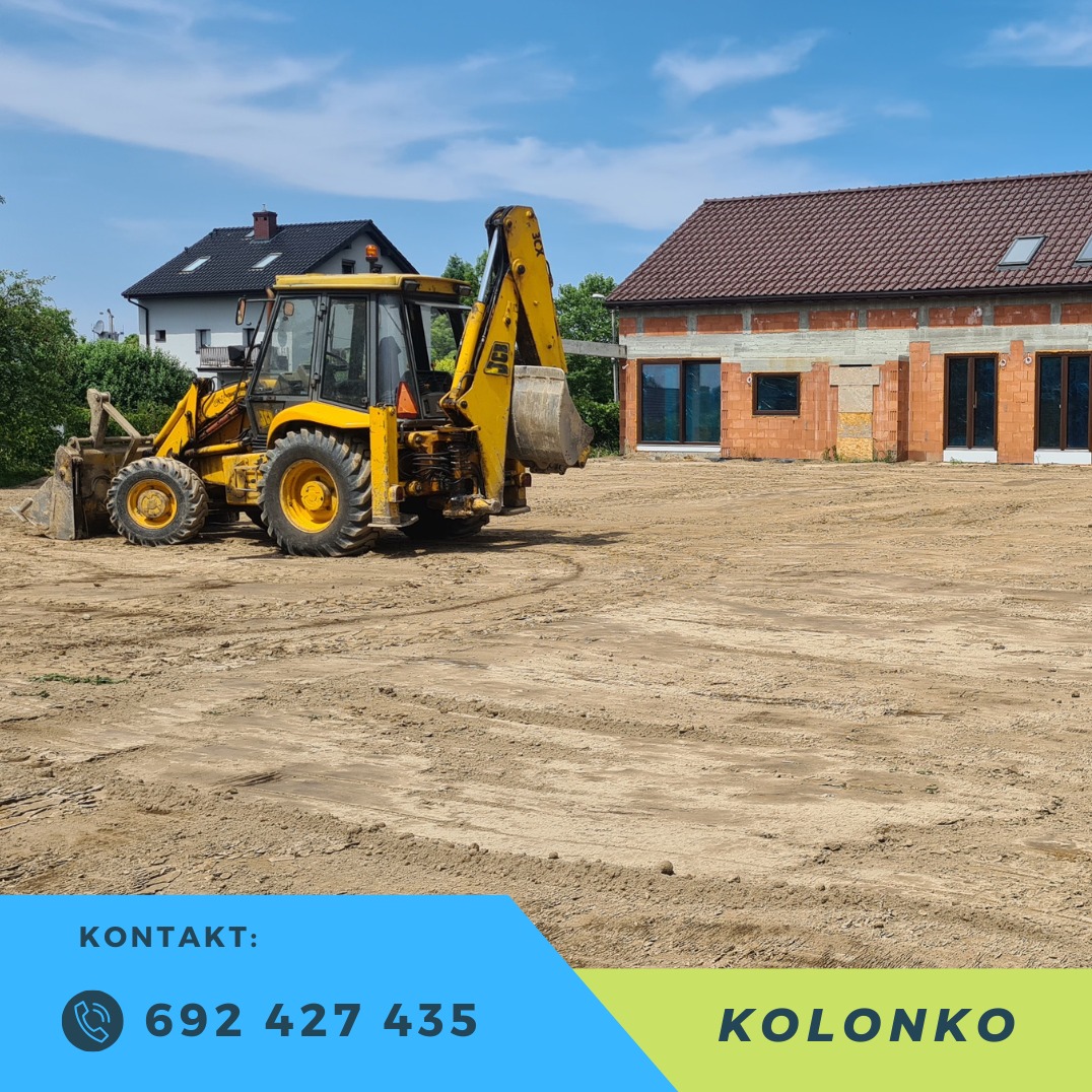 Żółta koparko-ładowarka na placu budowy, w tle dom w trakcie budowy z cegły. Ślady opon na piasku. Reklama firmy z numerem telefonu.