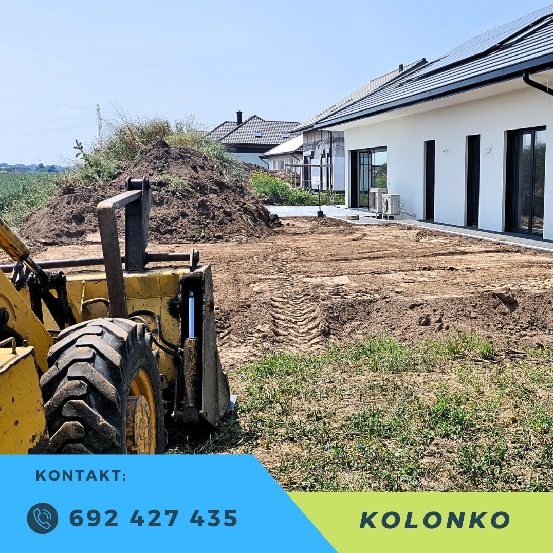 Żółta ładowarka kołowa na placu budowy z pryzmą ziemi i nowym domem w tle. Widoczne ślady opon na ziemi i częściowo zarośnięty teren.