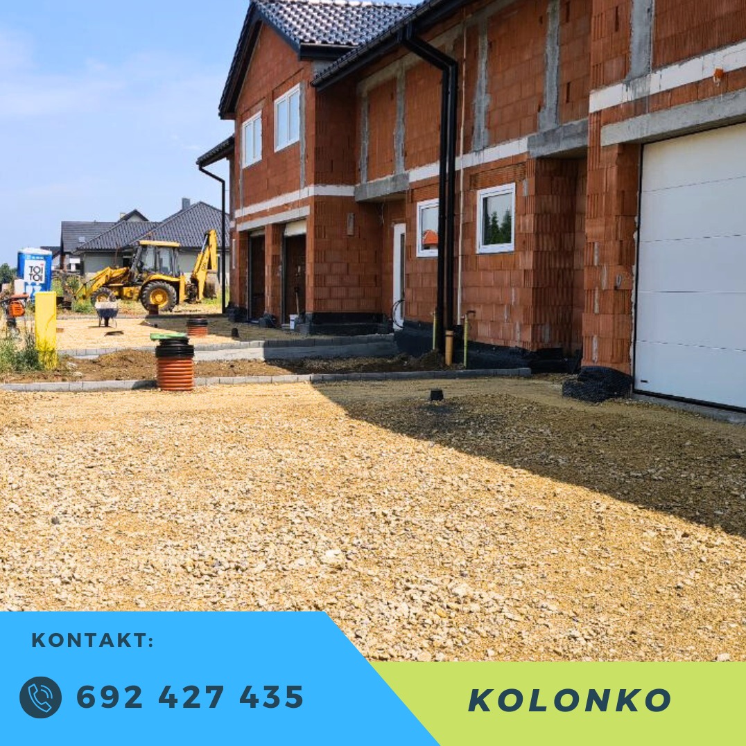 Budowa bliźniaka z utwardzonym terenem. Koparka w tle. Widoczne fundamenty i ściany z cegły. Utwardzona droga dojazdowa.