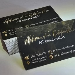 VisualLook Łukasz Rajkowski - Eleganckie, czarno-złote wizytówki z połyskującym, marmurkowym tłem i danymi kontaktowymi salonu kosmetycznego, ułożone w dwie stosy na jasnym podłożu.