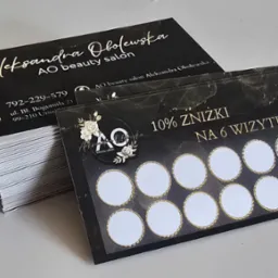 Stos wizytówek premium z czarnym tłem i złotymi napisami, obok karta lojalnościowa z 10% zniżką na 6 wizytę, dla salonu kosmetycznego.