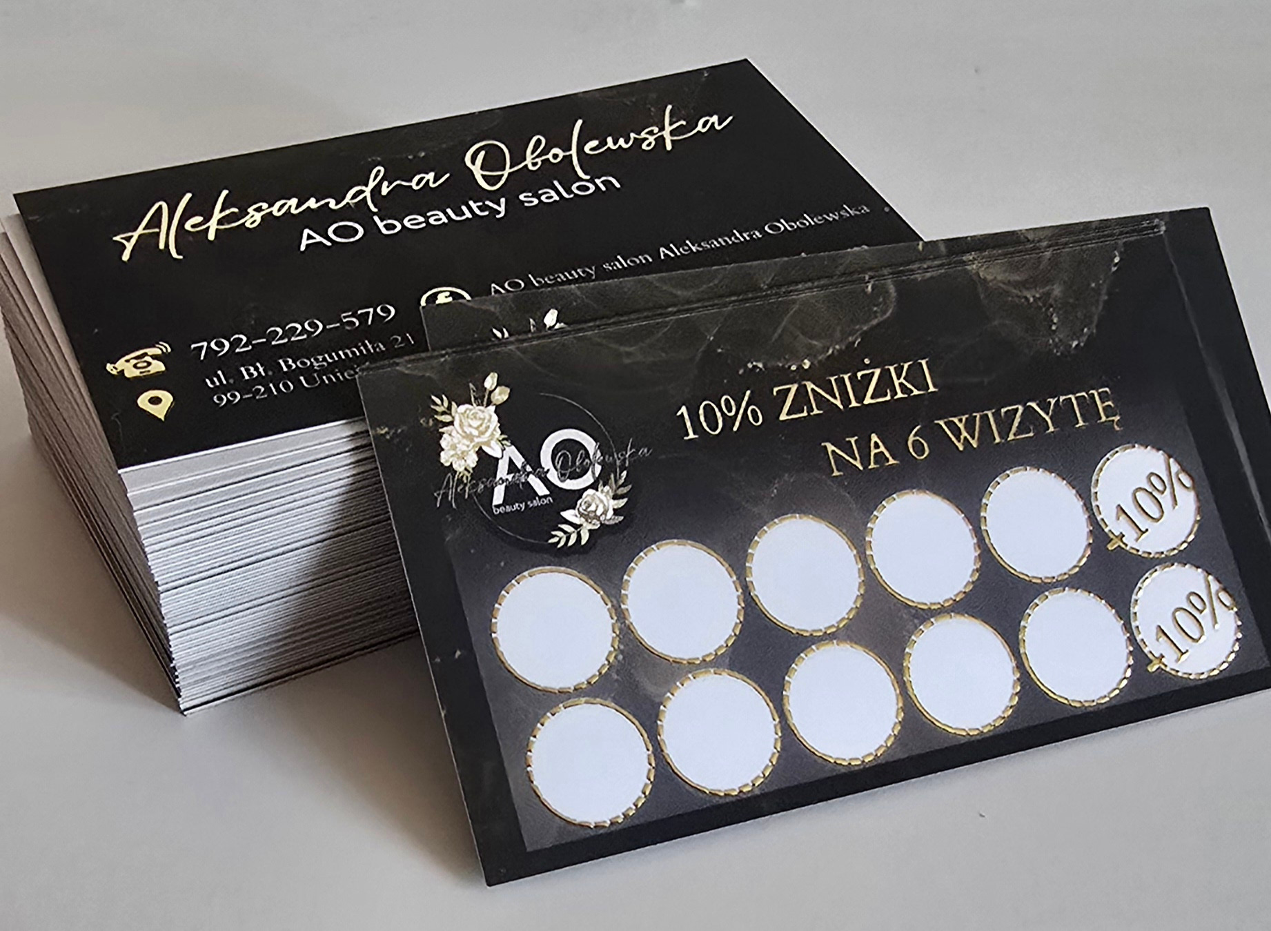 Stos wizytówek premium z czarnym tłem i złotymi napisami, obok karta lojalnościowa z 10% zniżką na 6 wizytę, dla salonu kosmetycznego.