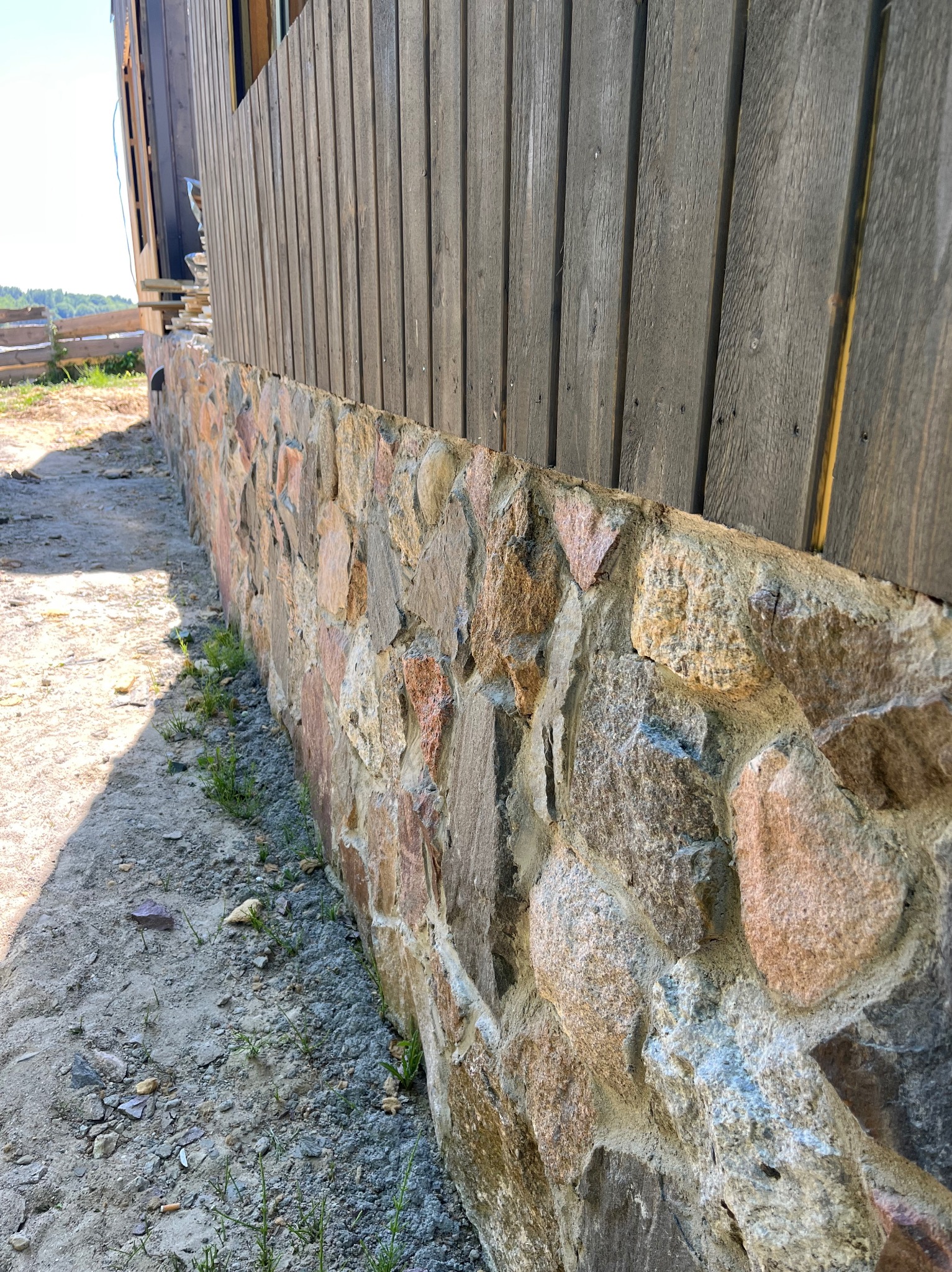 Fragment elewacji domu szkieletowego z drewnianą fasadą i kamienną podmurówką w ciepłych odcieniach, widoczny z bliska, w naturalnym oświetleniu.