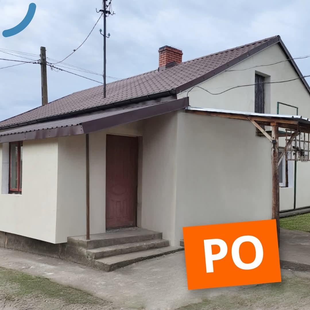 Ocieplony dom jednorodzinny z brązowym dachem, widok z zewnątrz, po remoncie. Na pierwszym planie pomarańczowy napis 'PO'.