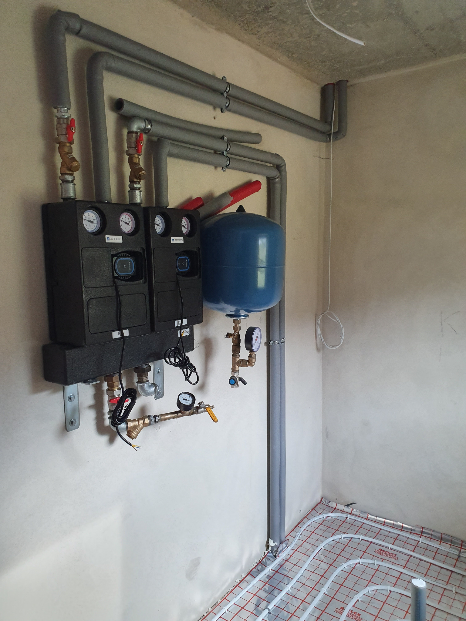 Instalacja grzewcza z rozdzielaczem Afriso, zbiornikiem wyrównawczym i rurami w izolacji, ogrzewanie podłogowe w trakcie montażu, surowe ściany.