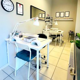 Gabinet Kosmetyki Laserowej i Stylizacji Paznokci Dorota Musidlak - Jasne wnętrze salonu z dwoma stanowiskami do manicure. Na ścianach certyfikaty i półki z lakierami. Białe meble, lampy i sprzęt kosmetyczny.
