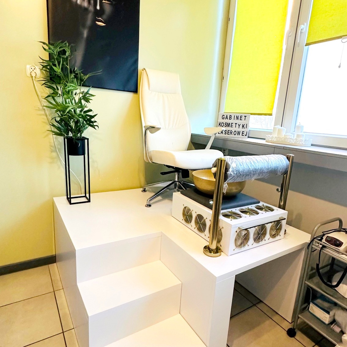 Jasne wnętrze salonu z fotelem, misą do pedicure i rośliną doniczkową. Minimalistyczny design i profesjonalny sprzęt.