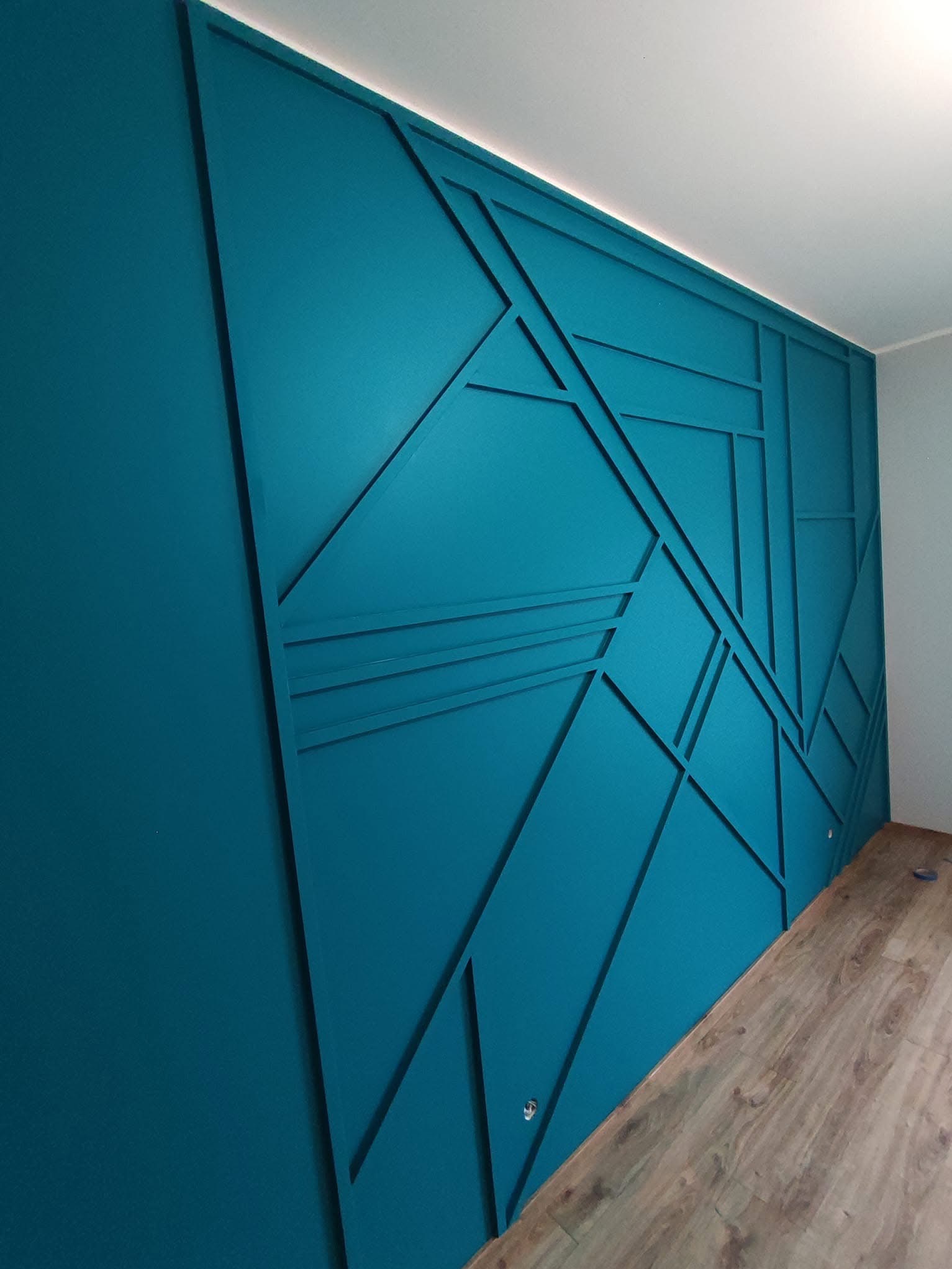 Turkusowa ściana z geometrycznym wzorem 3D, drewniana podłoga. Nowoczesny design wnętrza, wykończenie z listew dekoracyjnych.