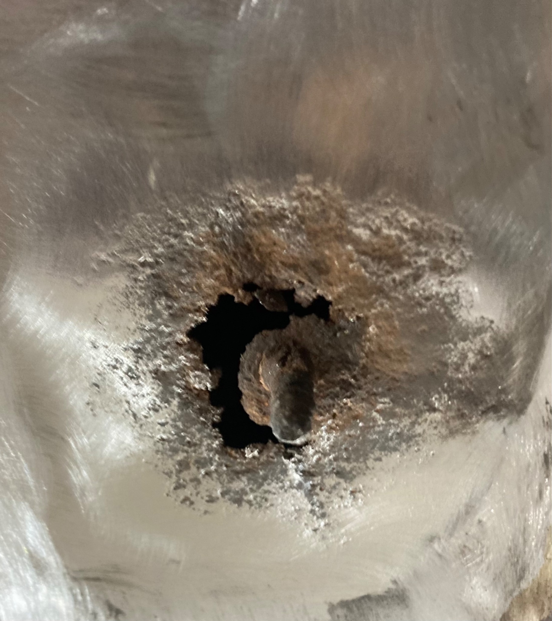 Korozja wokół metalowego elementu, prawdopodobnie śruby, na powierzchni z widocznymi śladami obróbki szlifierskiej. Widoczne ogniska rdzy i uszkodzenia materiału.