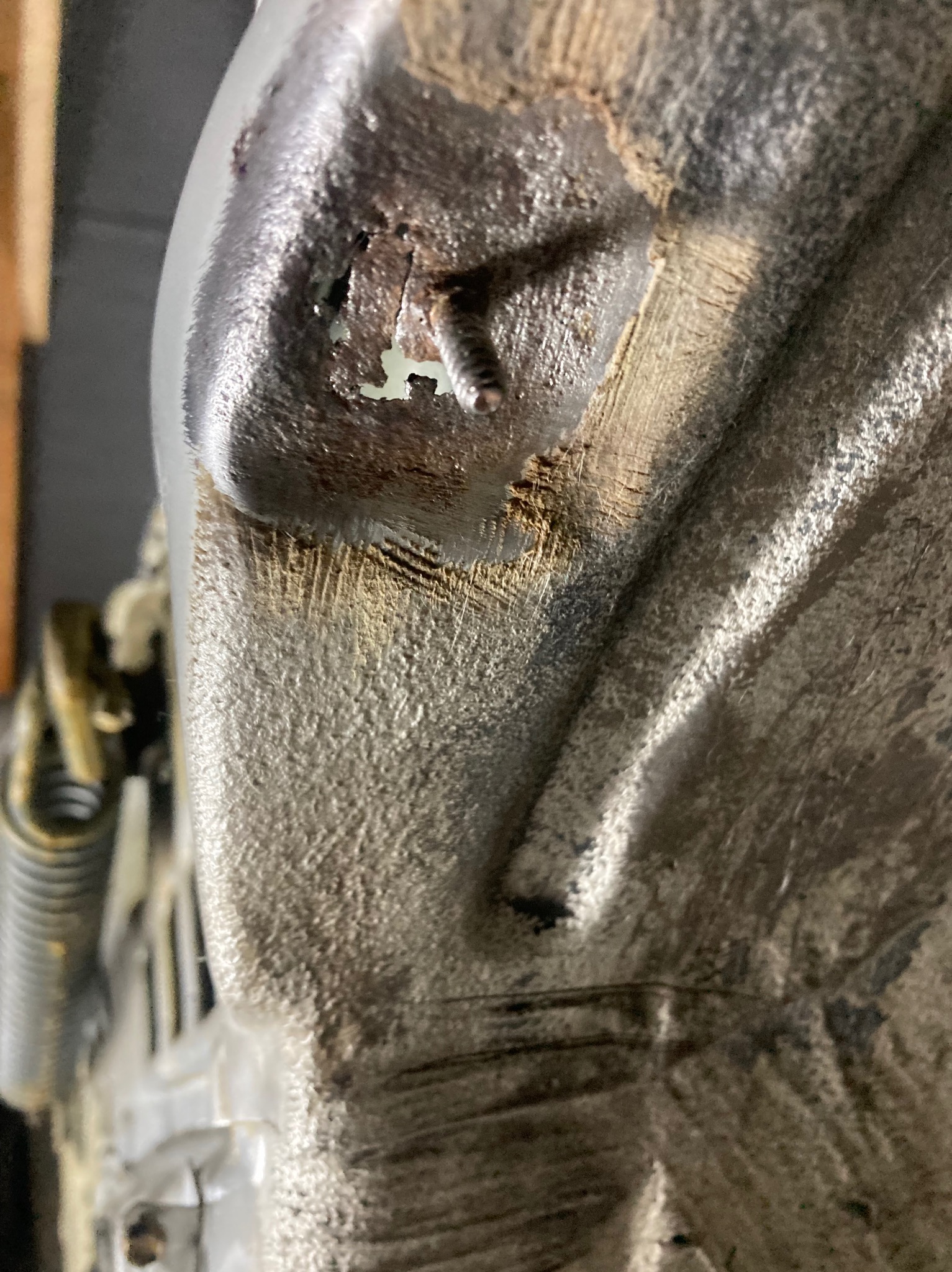 Detal skorodowanej karoserii pojazdu z widocznymi śladami rdzy i wcześniejszych napraw. Widoczne śruby i fragment podwozia. Szorstka faktura i nierówności powierzchni.