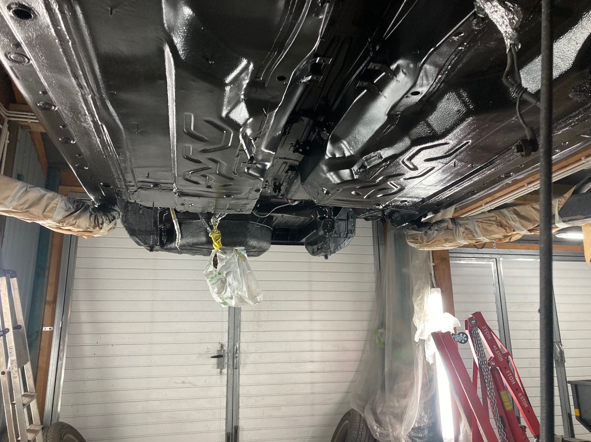 Podwozie auta po konserwacji antykorozyjnej, widoczne z dołu na podnośniku. Elementy zawieszenia, ramy i karoserii pokryte czarną, błyszczącą powłoką ochronną.