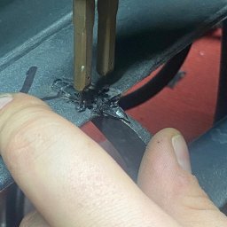 KONSPAW PAWEŁ WDANIEC MOBILNY SERWIS - Zbliżenie na proces spawania plastiku z użyciem spawarki, widoczne dłonie operatora i stopiony plastik na szarej powierzchni, z czerwonym elementem w tle.