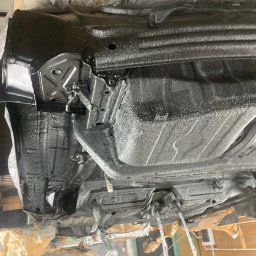 KONSPAW PAWEŁ WDANIEC MOBILNY SERWIS - Podwozie auta po konserwacji antykorozyjnej, zabezpieczone czarną powłoką. Widoczny podnośnik warsztatowy i elementy zabezpieczone folią. Detal z bliska.