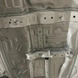 Szare, świeżo pomalowane podwozie samochodu z widocznymi elementami konstrukcyjnymi i otworami. Ujęcie z dołu, ukazujące detale po konserwacji.