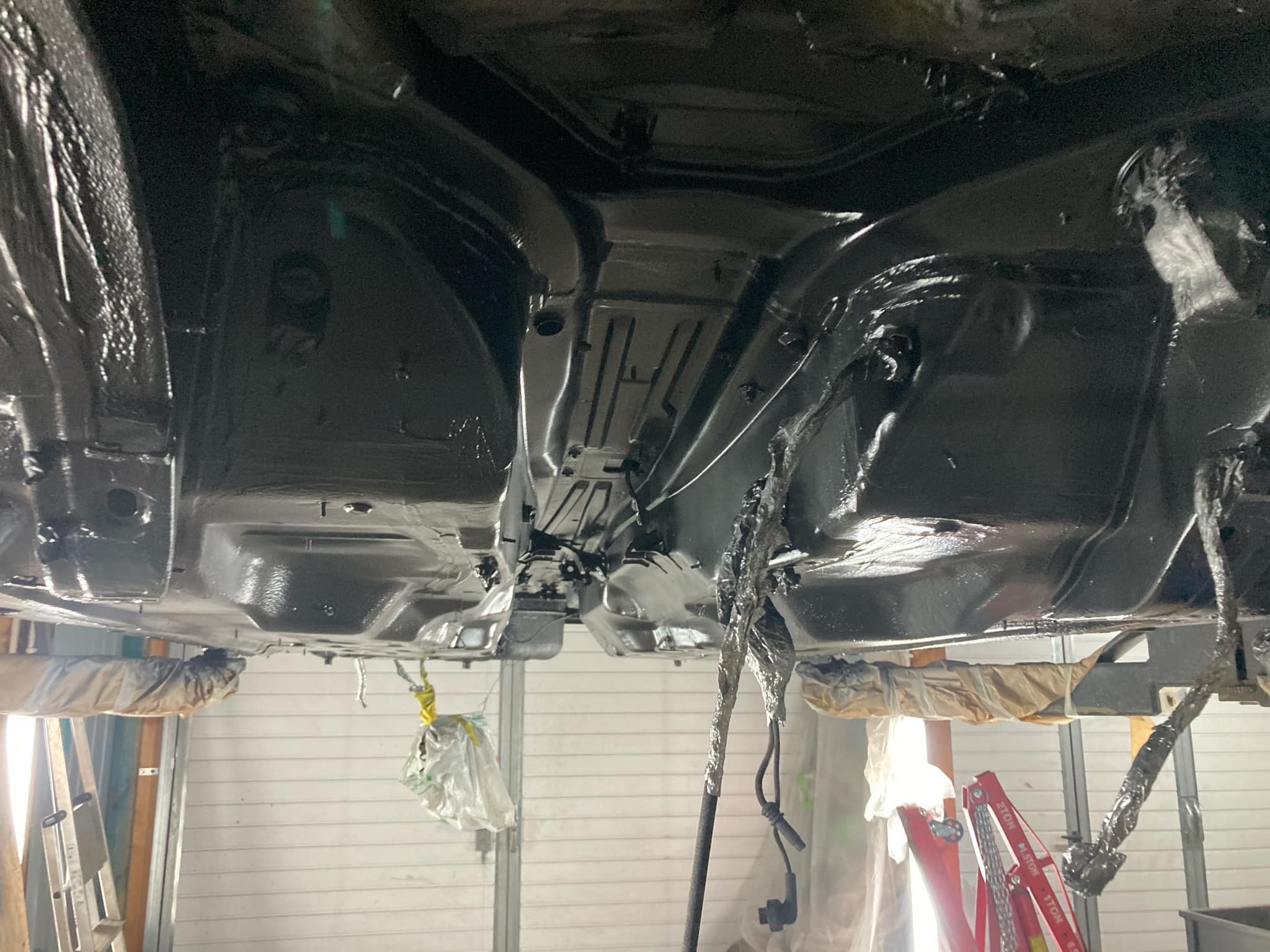 Podwozie auta po konserwacji antykorozyjnej, widok od spodu, zabezpieczone elementy w Wieliczce. Błyszcząca, czarna powłoka, detale zawieszenia.