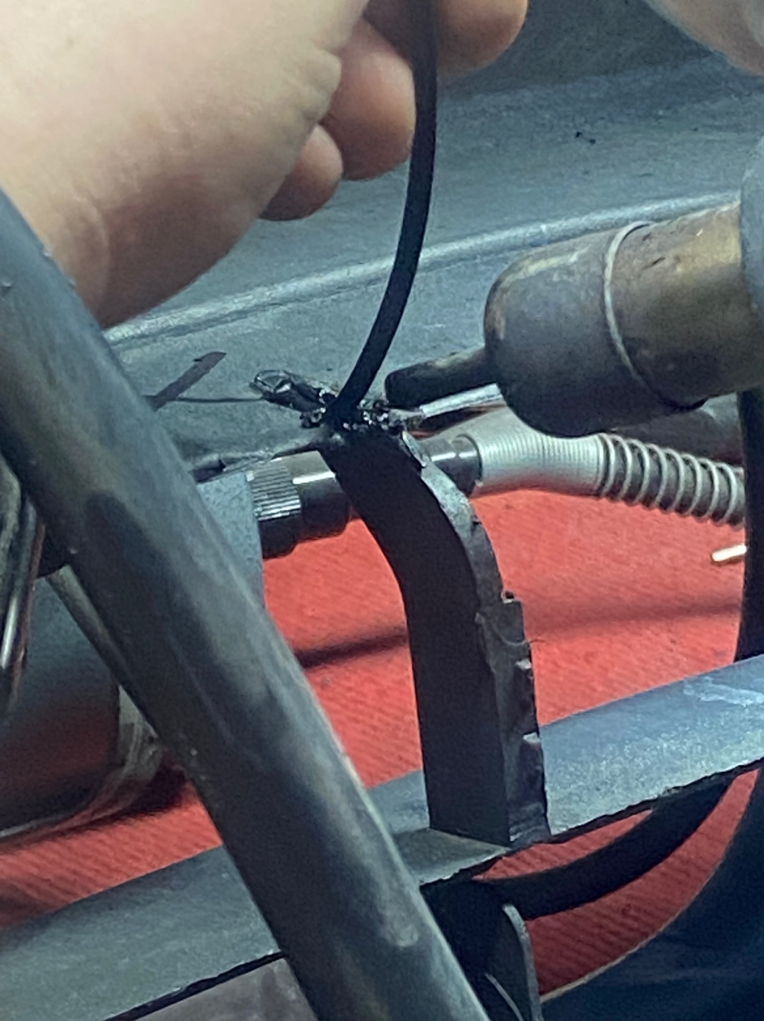 Detal spawania metalowego elementu konstrukcyjnego. Widoczne narzędzie spawalnicze i ręka spawacza. Precyzyjne łączenie elementów.