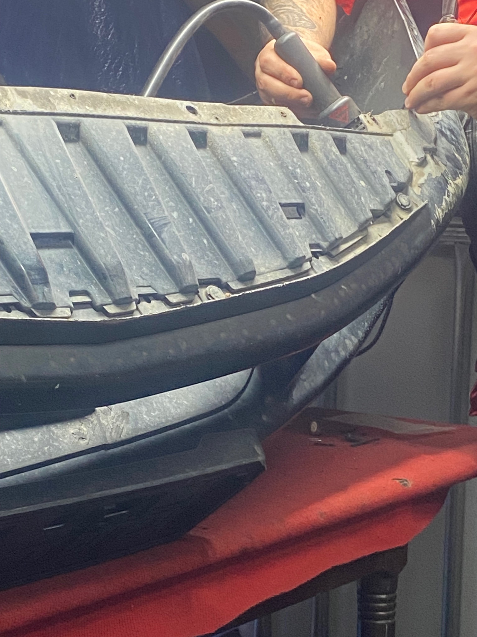 Naprawa plastikowego elementu pojazdu szlifierką oscylacyjną. Drobne wióry i pył w miejscu pracy. Widoczne dłonie pracownika.