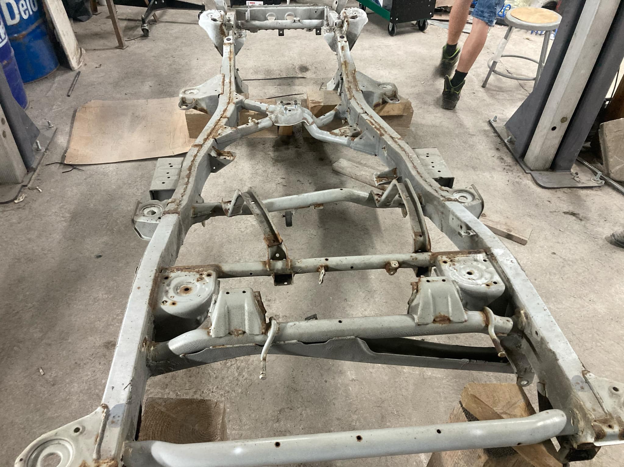 Oczyszczona rama pojazdu na drewnianych podporach w warsztacie, widoczne ślady korozji, przygotowana do dalszej konserwacji. Ujęcie z góry.