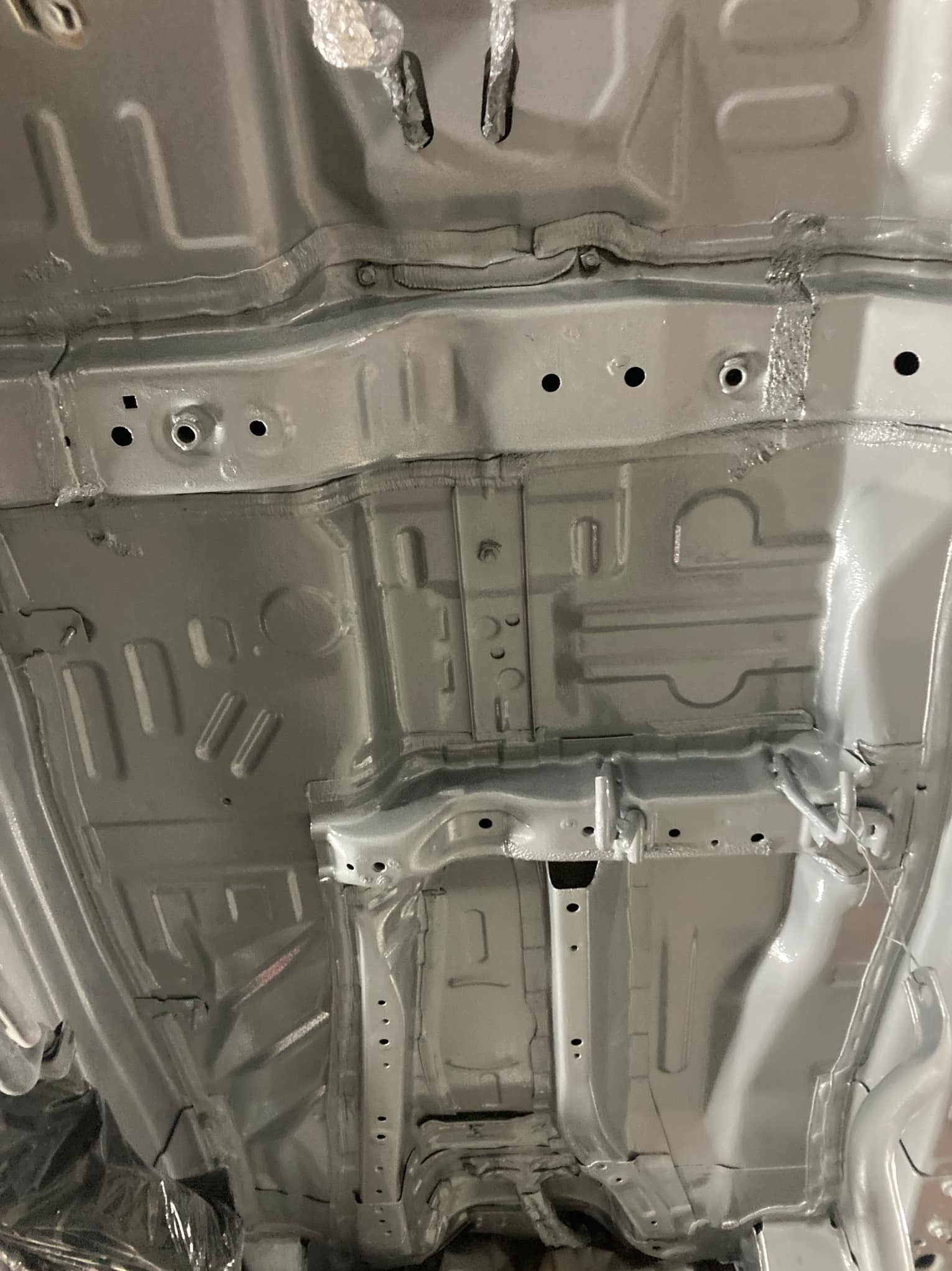 Szare, świeżo pomalowane podwozie samochodu z widocznymi elementami konstrukcyjnymi i otworami. Ujęcie z dołu, ukazujące detale po konserwacji.