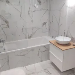 Wykończona łazienka z wanną obudowaną płytkami imitującymi marmur, białą szafką pod umywalką z drewnianym blatem i chromowaną armaturą.