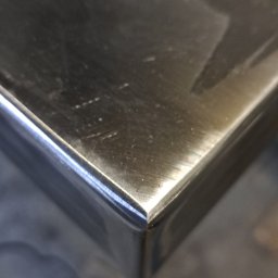 Arkadiusz Blat - Detal narożnika spawanej konstrukcji ze stali nierdzewnej, widoczny z bliska pod kątem, z refleksami światła na gładkiej powierzchni metalu.
