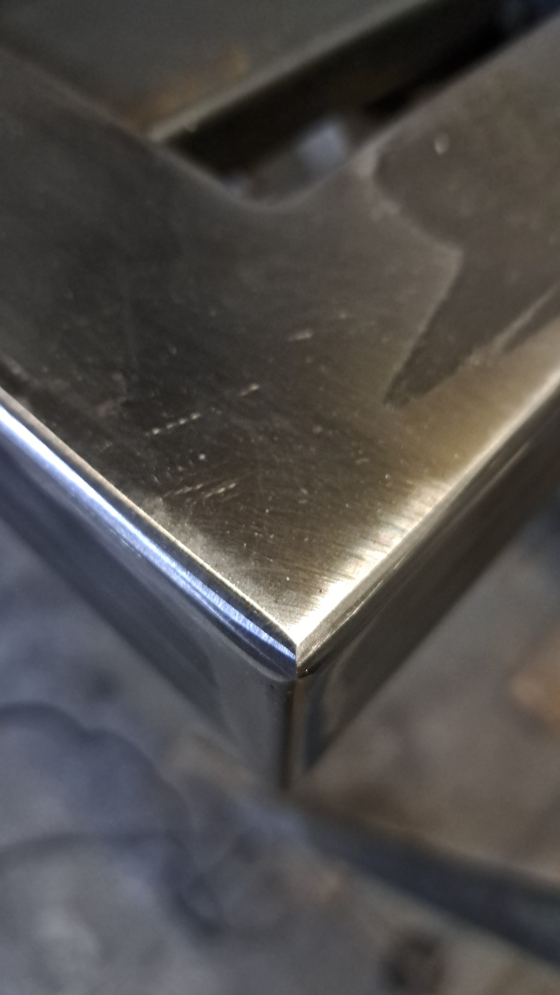 Detal narożnika spawanej konstrukcji ze stali nierdzewnej, widoczny z bliska pod kątem, z refleksami światła na gładkiej powierzchni metalu.