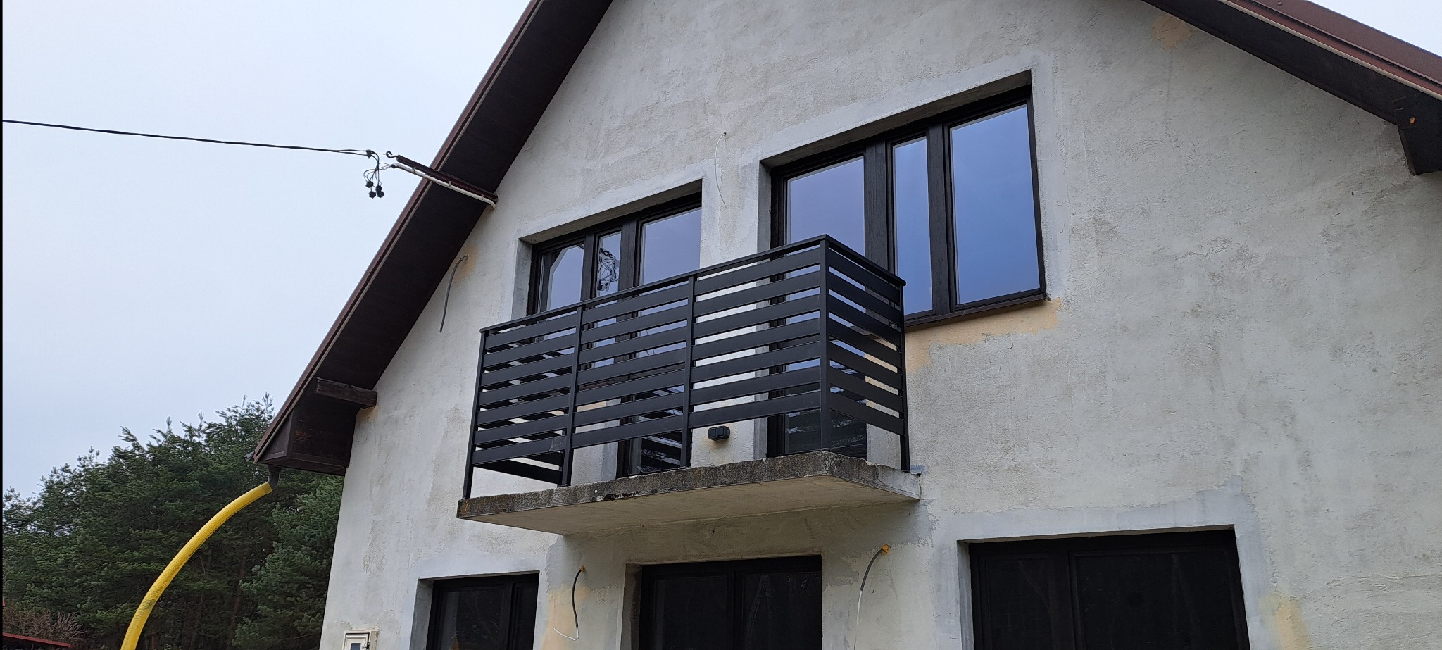 Czarna, pozioma konstrukcja zabezpieczająca balkon w Kolbuszowej, zamontowana na szarym budynku z ciemnymi oknami. Widok z dołu na elewację.