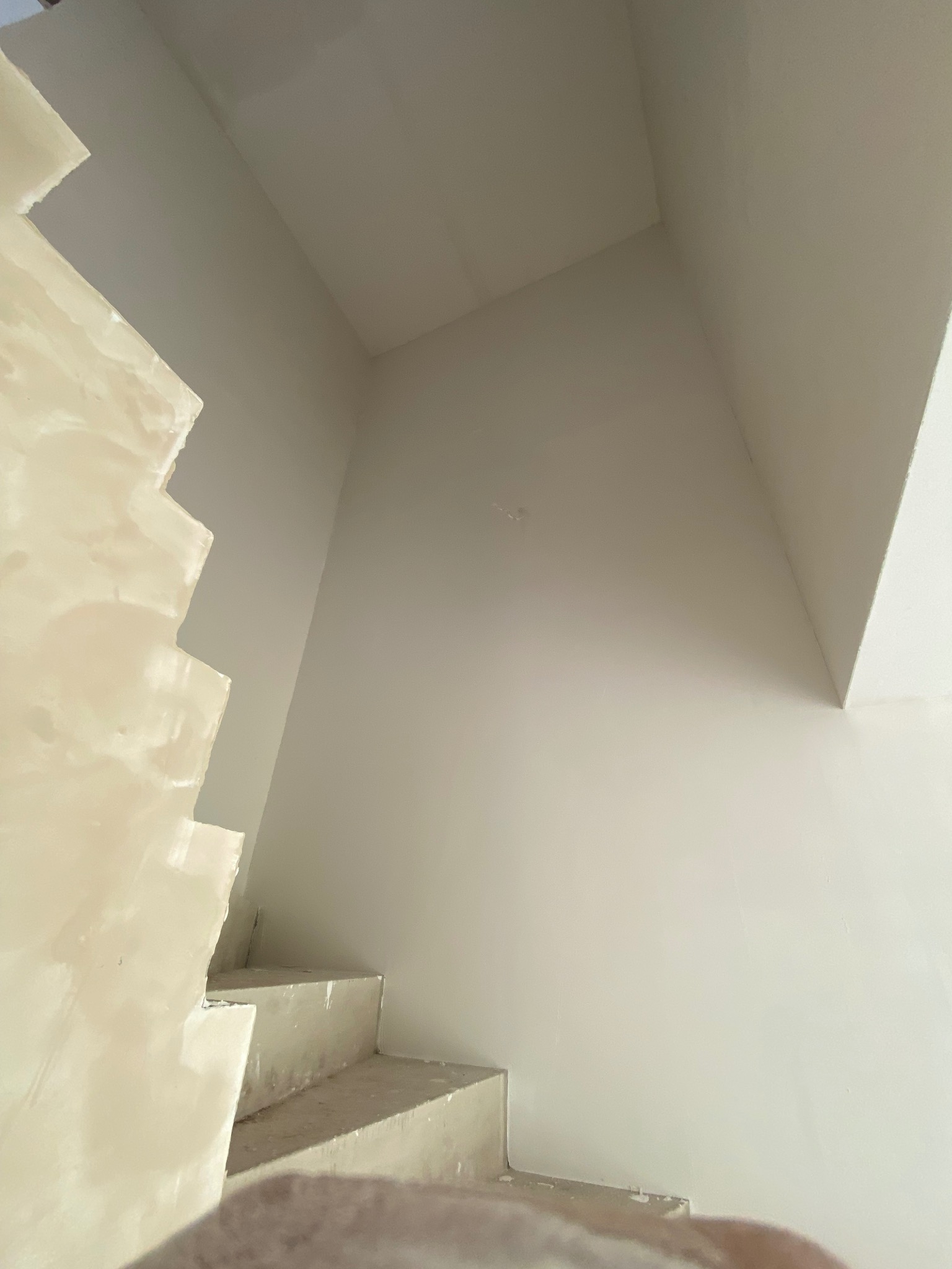 Ściana i schody w trakcie szpachlowania, widoczne nierówności i nałożona warstwa gładzi. Jasne wnętrze w trakcie prac wykończeniowych. Ujęcie z dołu.