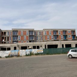 PRZEDSIĘBIORSTWO HANDLOWO-USŁUGOWE MAGDALENA MATUSIAK - Budynek w stanie surowym z zamontowanymi oknami, widoczne banery reklamowe dewelopera, samochód na parkingu. Ujęcie z poziomu ulicy.