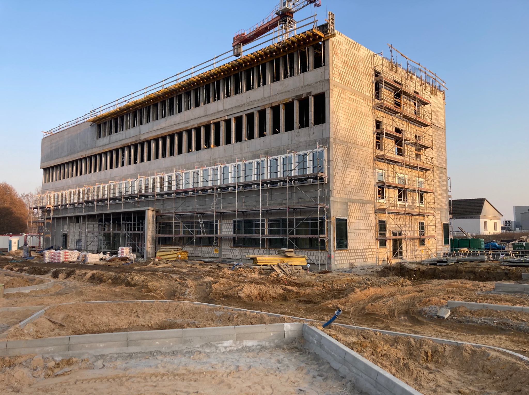 Budynek w trakcie budowy z widocznymi oknami na rusztowaniach, ceglana elewacja i żuraw budowlany w tle, teren budowy w stanie surowym.