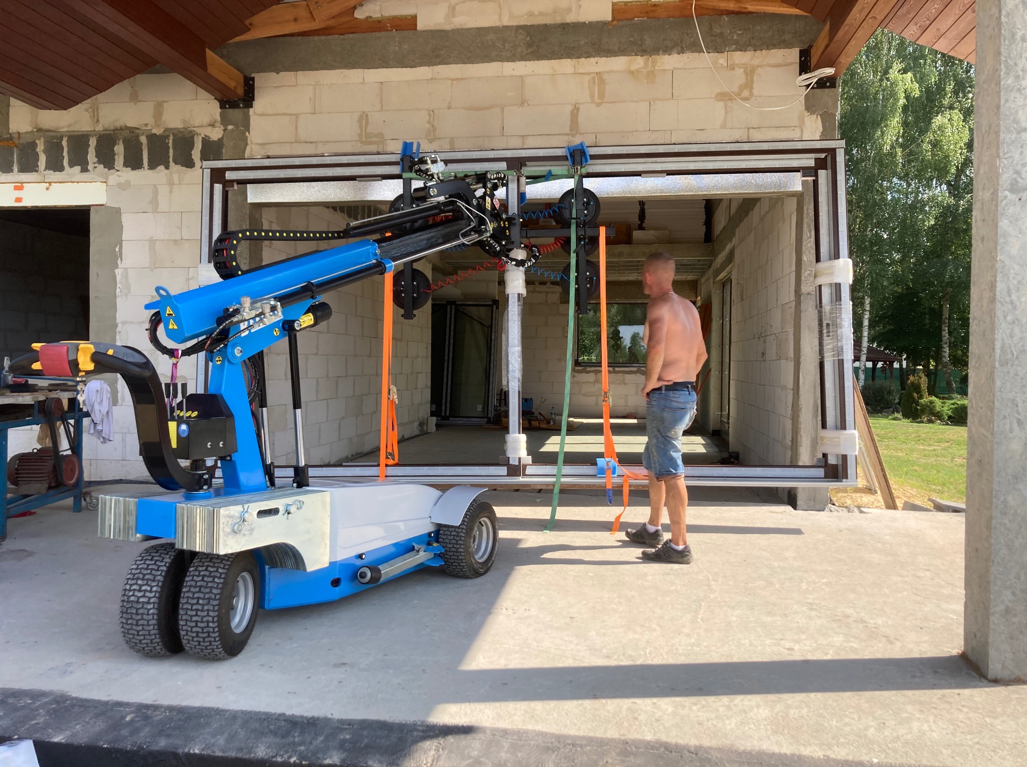 Montaż okna panoramicznego za pomocą specjalistycznego podnośnika w surowym stanie budynku. Widoczny pracownik nadzorujący proces.