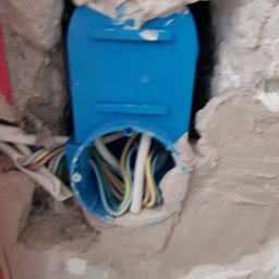 Fresh Art - Niebieska puszka instalacyjna w surowej ścianie z widocznymi przewodami elektrycznymi w różnych kolorach. Fragment instalacji w trakcie prac.