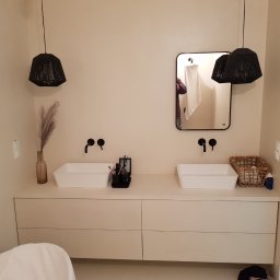 Fresh Art - Jasna łazienka z dwoma umywalkami nablatowymi, czarną armaturą i lampami w stylu boho. W lustrze odbija się fragment osoby. Minimalistyczny design.