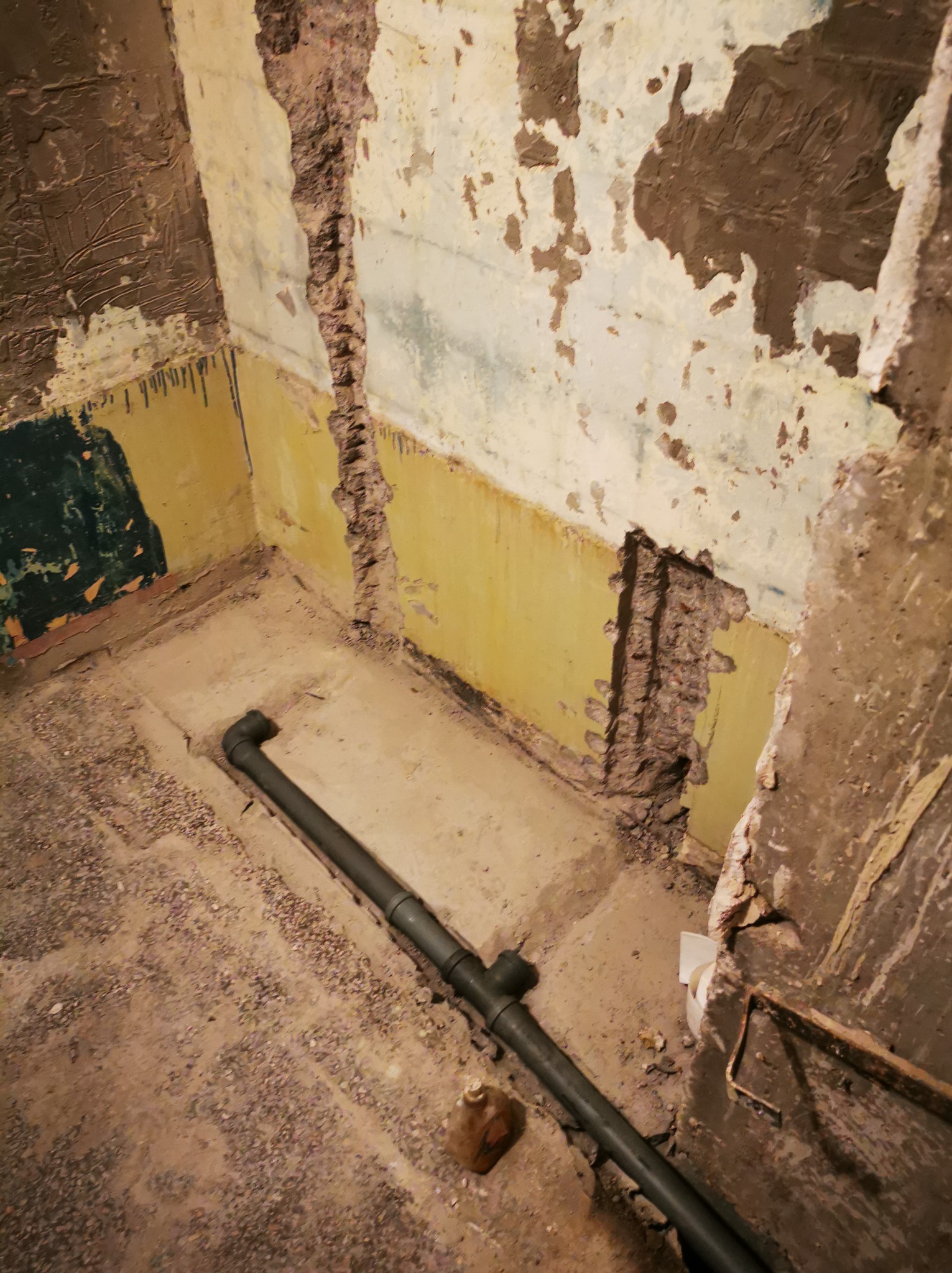 Demontaż starej łazienki: fragment ściany z odsłoniętą strukturą, rura kanalizacyjna na podłodze. Przygotowanie do remontu, widoczne ślady po starych płytkach.