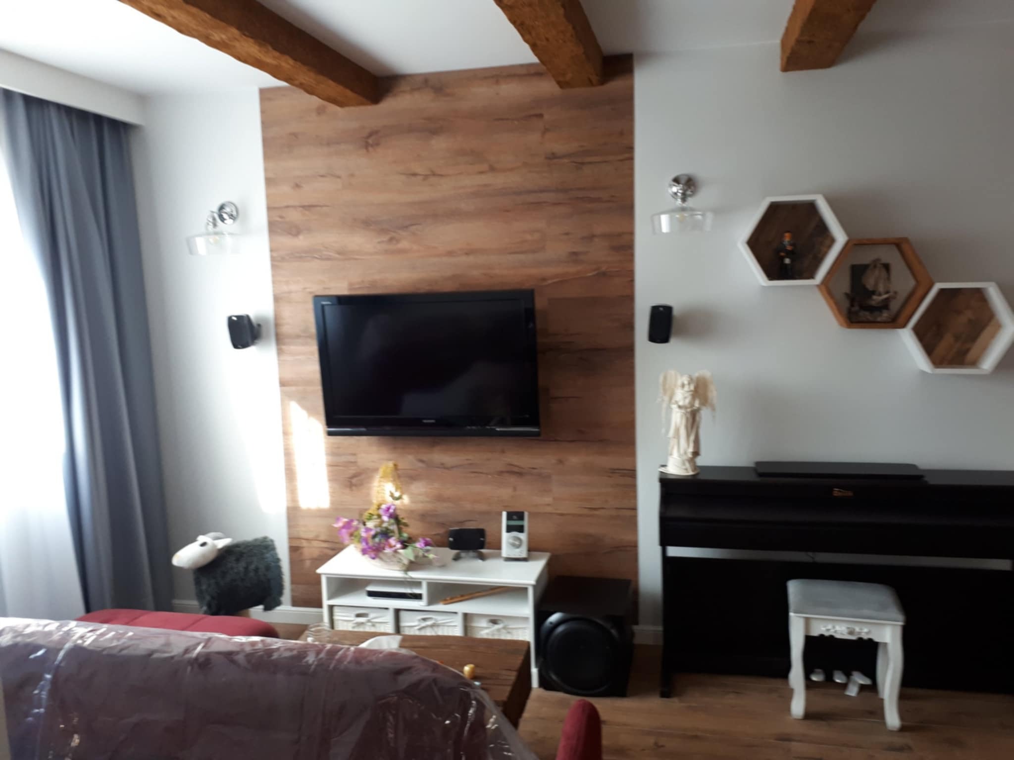 Salon z panelami winylowymi na ścianie, świeżo szpachlowanymi i pomalowanymi ścianami oraz sufitem. Widoczne drewniane belki stropowe i dekoracje ścienne.