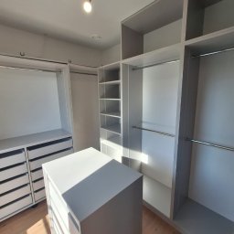 Paulina Folwa - Jasna, przestronna garderoba z szufladami i półkami, oświetlona punktowym światłem, z drewnianą podłogą i widocznym światłem słonecznym.