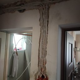 Elektro System - Białe kable elektryczne prowadzone w bruzdach ściany, widoczne puszki instalacyjne. Remont instalacji elektrycznej w trakcie realizacji.
