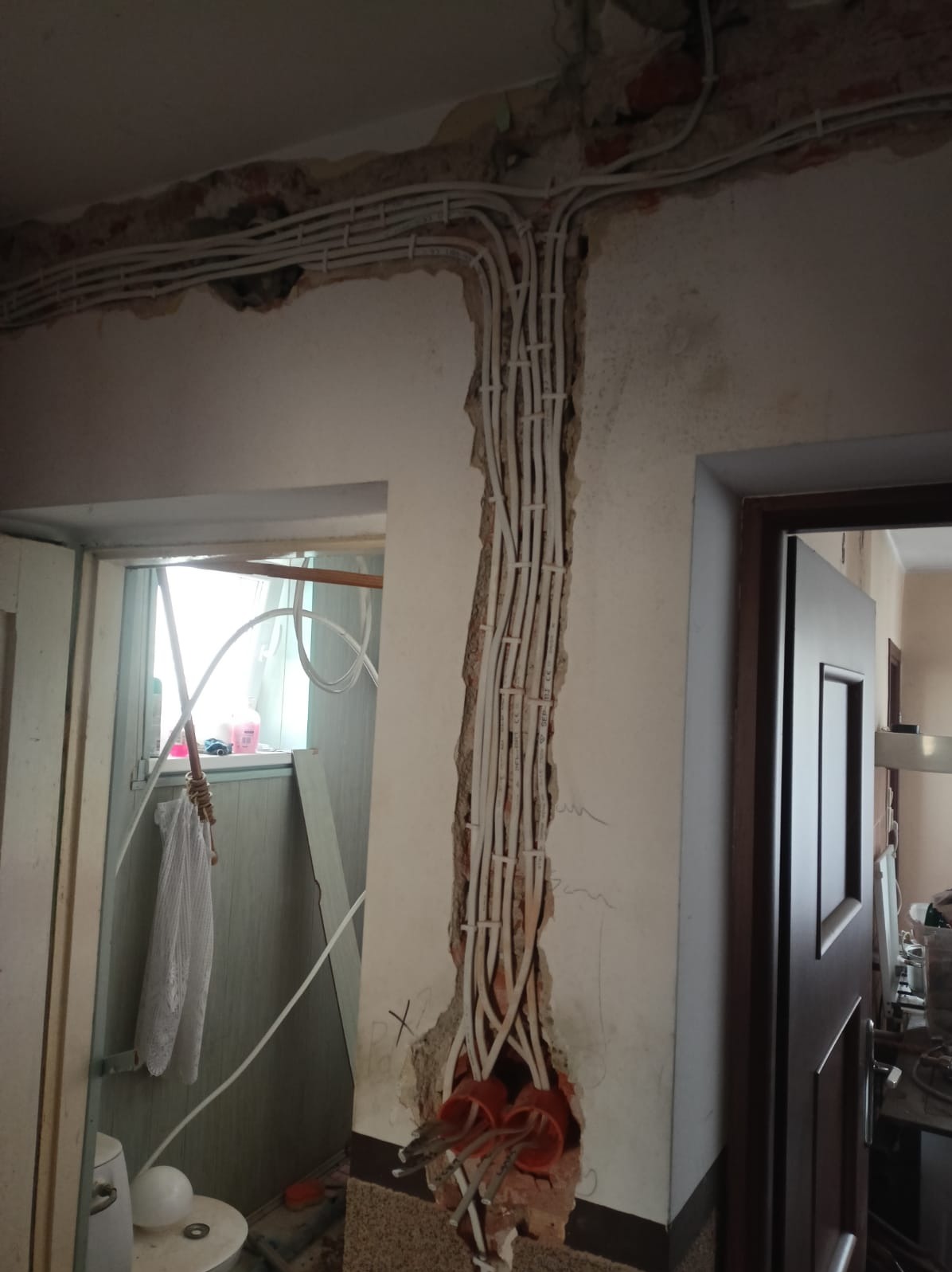 Białe kable elektryczne prowadzone w bruzdach ściany, widoczne puszki instalacyjne. Remont instalacji elektrycznej w trakcie realizacji.
