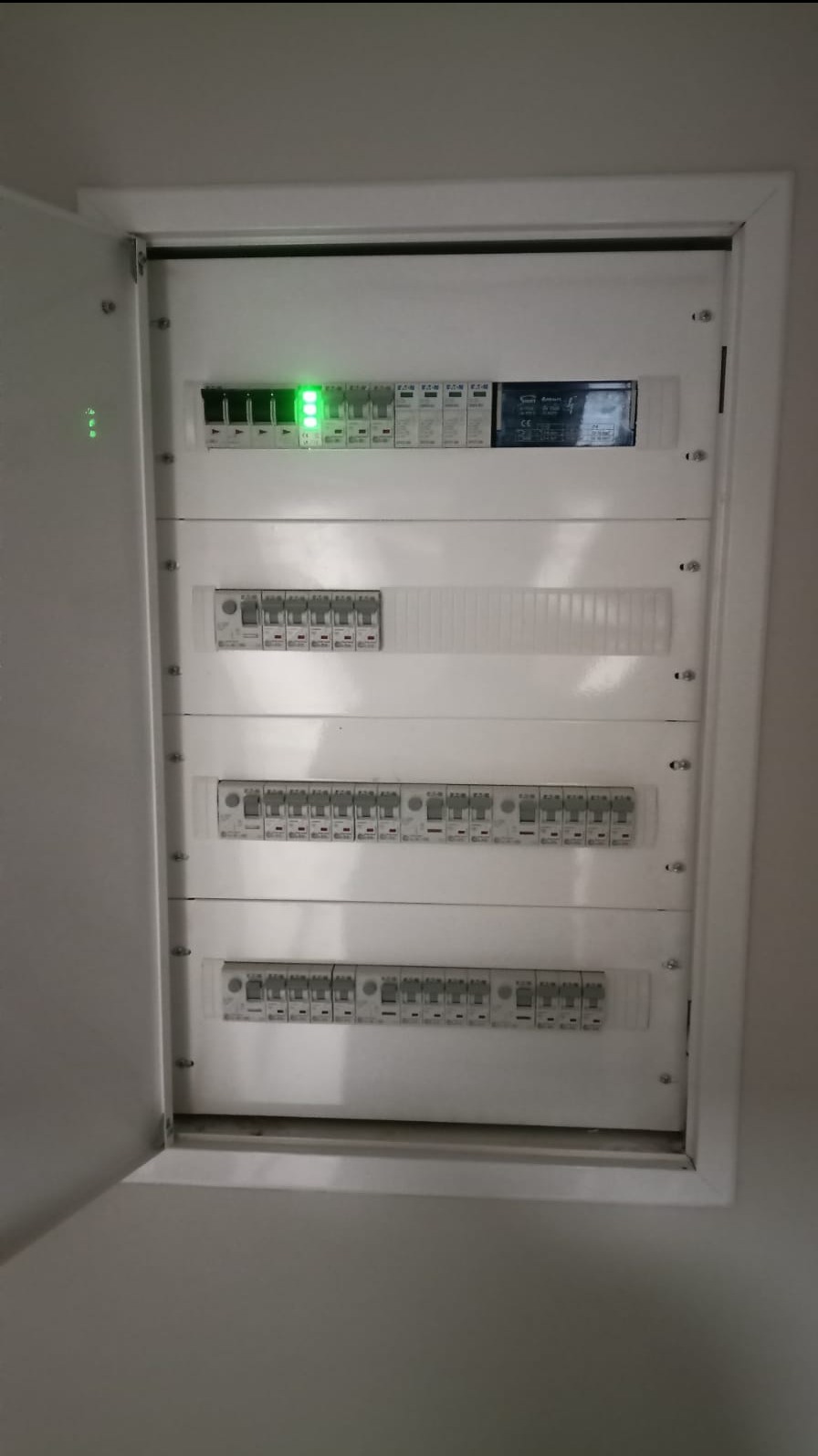 Otwarta, biała szafka rozdzielcza z bezpiecznikami i zielonymi diodami LED, zamontowana na ścianie, widok z bliska.