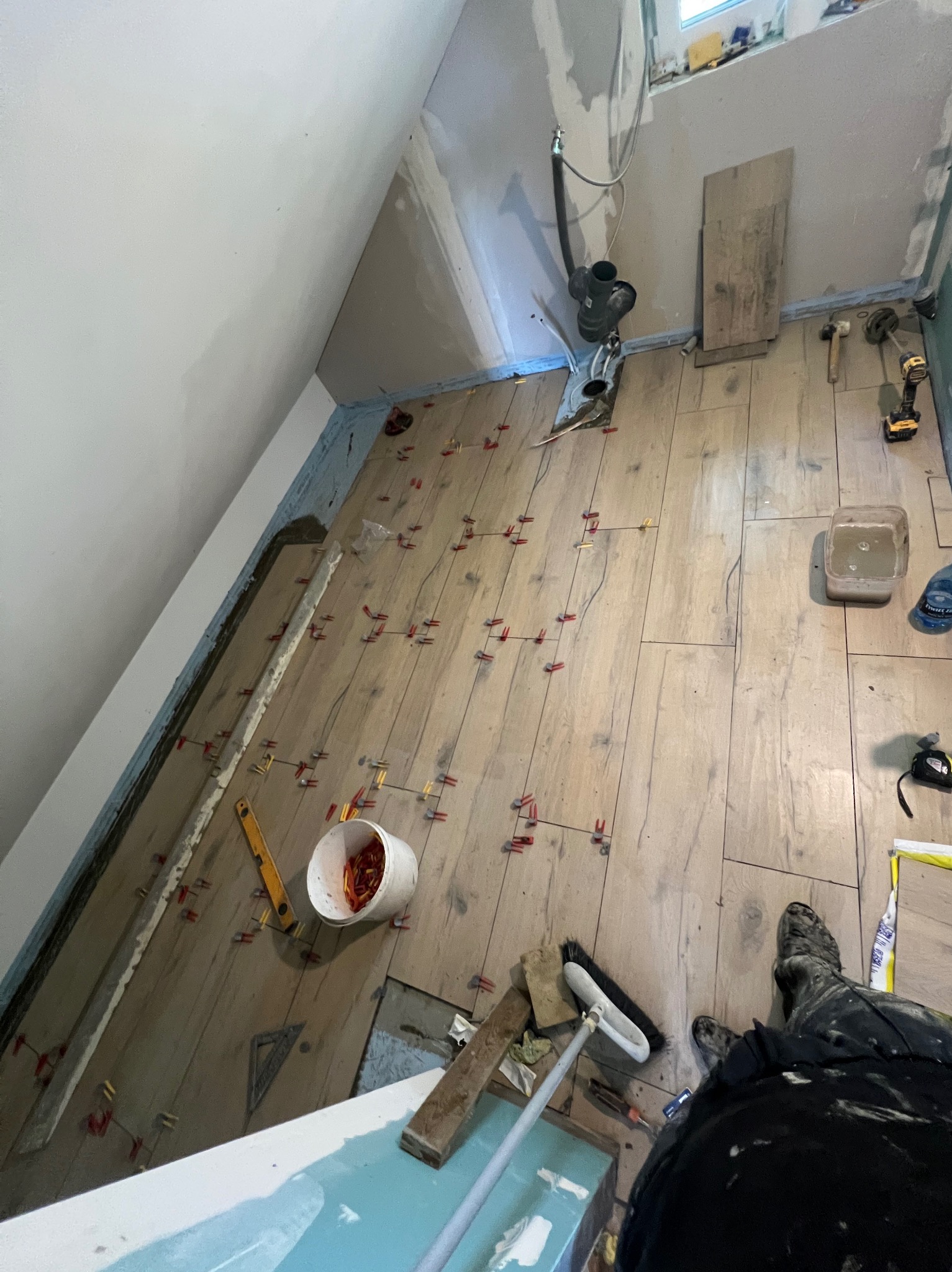 Układanie drewnopodobnych płytek w łazience na poddaszu. Widoczne narzędzia glazurnicze i krzyżyki dystansowe. Ujęcie z góry, w kadrze fragment osoby.