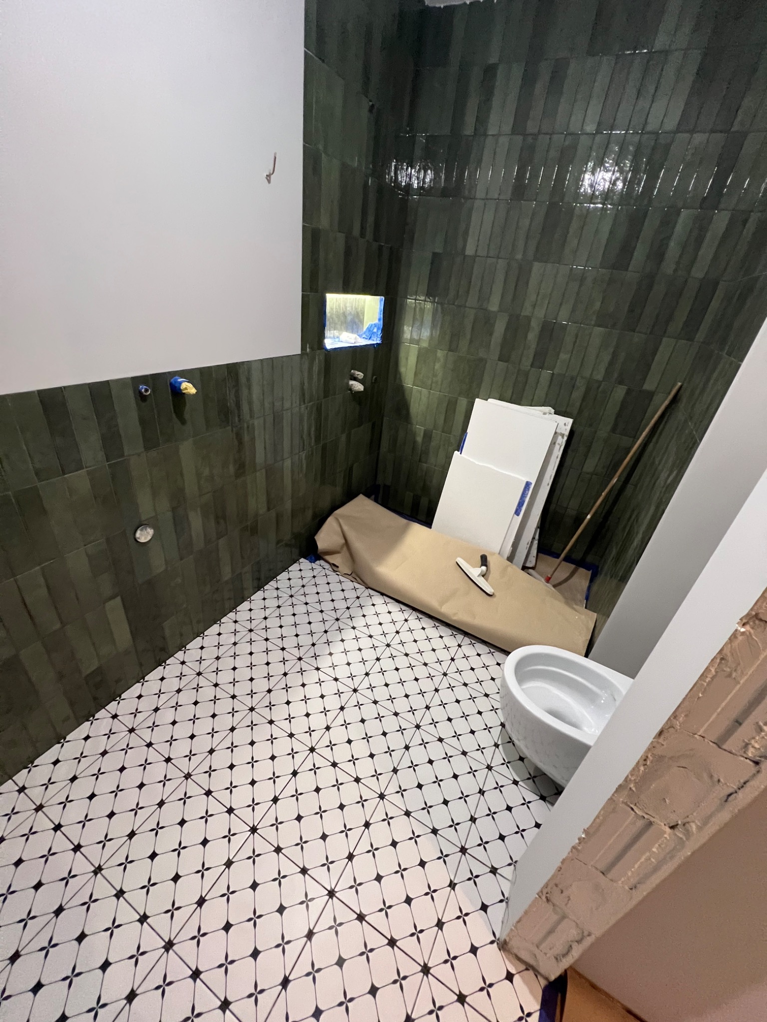 Łazienka w trakcie remontu: ułożona podłoga z wzorem, zielone płytki na ścianach, biała ceramika sanitarna, narzędzia i materiały budowlane. Widok z góry.