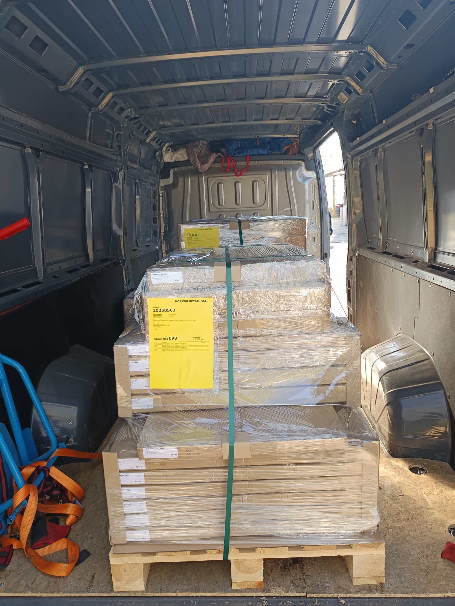 Wnętrze busa z załadowanymi paletami z towarem zabezpieczonym folią i taśmami. Widoczne akcesoria do transportu i etykiety 'Not for retail sale'.