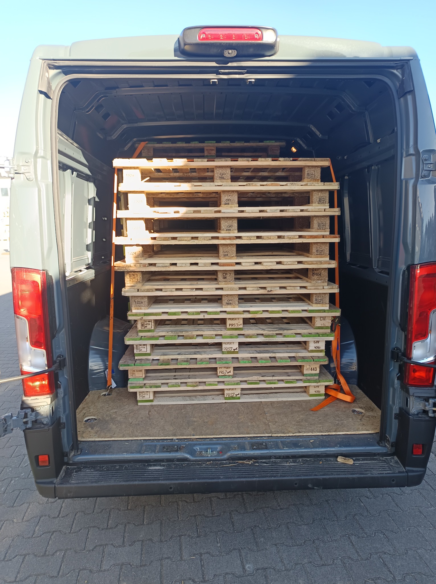 Wnętrze busa załadowane paletami, zabezpieczone pomarańczowymi pasami transportowymi. Widok z tyłu pojazdu, otwarte drzwi.